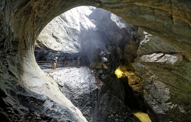 Beautiful scene of a mysterious cave sculptured by Trummelbach Waterfall (Trummelbachfalle) in Lauterbrunnen Valley Switzerland, with sunlight from above & a tourist admiring the view from the tunnel