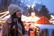 Woman Looks At Night Christmas City. Girl On Background Of Carousels And Amusement Park In Winter