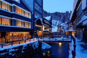 Wall Mural - Night scenery of Ginzan Onsen, a famous Japanese hot spring town in Obanazawa, Yamagata, Japan, with bridges over a stream flanked by antique wooden buildings after heavy snowfalls in cold winter