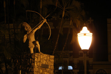 Canvas Print - Closeup shot of a lantern illuminating in the darkness with a statue in the background