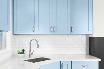 Detail of a kitchen with light blue cabinets, white granite countertop, subway tile backsplash, and a light hanging above a window.