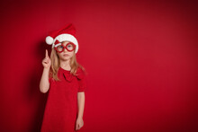Serious Girl In Christmas Clothes Raised Her Finger Up Stands On Red Background
