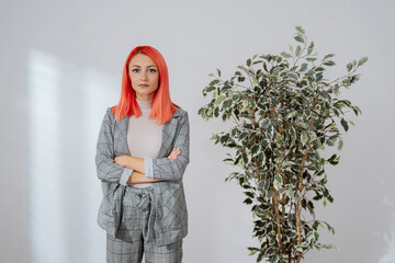 Elegant pink-haired woman stands against white wall in empty room, girl has arms crossed over chest she smiles at camera real estate agent insurance adjuster corporate office worker businesswoman