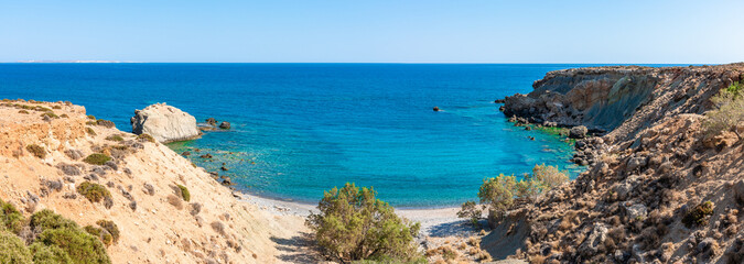 Wall Mural - Unique panoramic view of secluded remote bay pebble beach at Mediterranean Makrigialos summer resort southeast coast Crete Greece. Blue sky, crystal clear turquoise waters. Travel destination concept