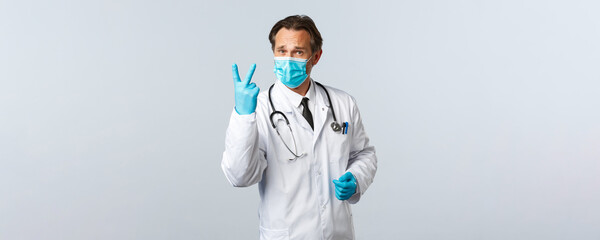 Covid-19, preventing virus, healthcare workers and vaccination concept. Serious concerned doctor in medical mask and gloves show number two, twice as prescribe medication, white background