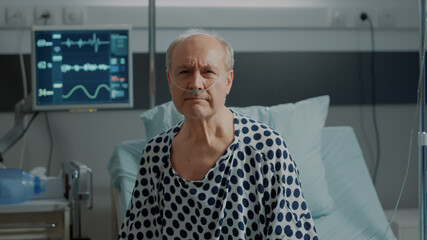portrait of elder patient with nasal oxygen tube standing on bed in hospital ward at medical clinic.