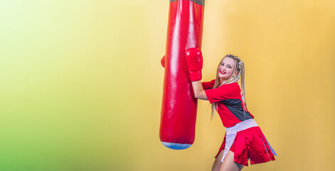 Sticker - Young happy girl kickboxer stands next to punching bag, holds it with hands and looks into camera