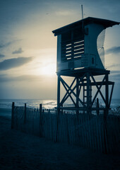 Canvas Print - Vertical shot of a lifeguard pier on the beach under a clear sky at sunrise