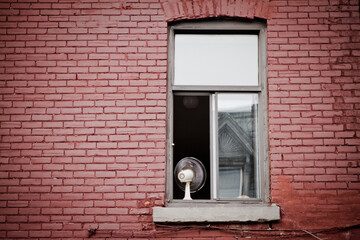 Canvas Print - Fan on a windowsill of an open window of a brick building