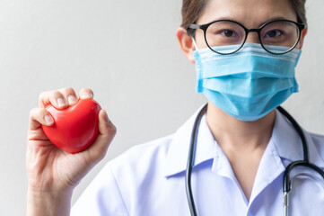 Wall Mural - Asian healthcare worker holding and squeezing a red heart toy in her hand. Conceptual of healthcare and medical service.