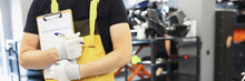 Auto Mechanic Locksmith In Yellow Uniform Stands In Car Repair Shop Closeup
