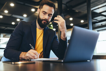 Young businessman writing notes during a phone call