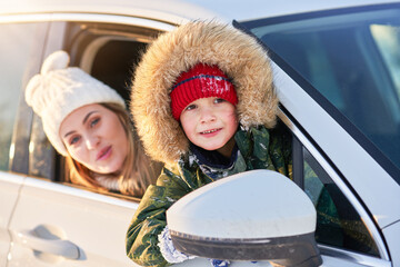 Young happy boy with mother in the car during winter