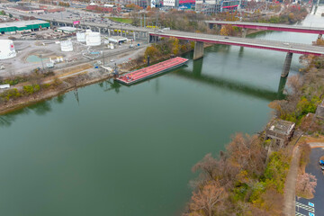 an aerial shot of the silky green waters of the Cumberland River with a freeways over the water and a barge on the water with buildings and autumn colored trees on the banks in Nashville Tennessee USA