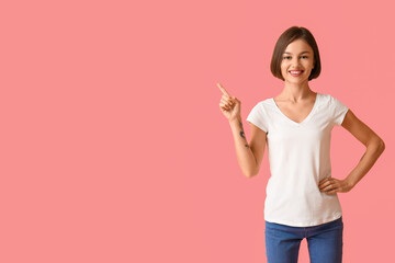 Wall Mural - Beautiful young woman in stylish t-shirt pointing at something on color background