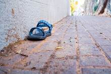 An Abandoned Sandal On A Sidewalk Next To A Wall