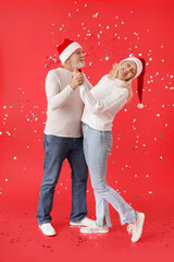 Poster - Happy dancing mature couple in Santa hats on color background