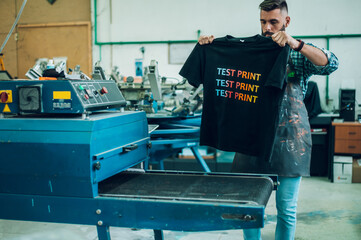 Male worker using a drying oven for t-shirt in a workshop