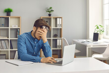 Stressful Office Job Finally Turns Young Man Into A Burnout. Stressed, Tired, Exhausted Male Worker Overwhelmed With Problems Sitting At Working Desk With Laptop Computer And Holding Hand On His Face