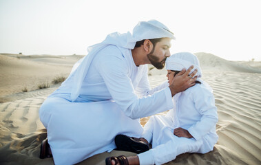 Wall Mural - Father and son spending time in the desert on a safari day. Arabian family from the emirates wearing the traditional white dress. Concept about lifestyle and middle eastern cultures