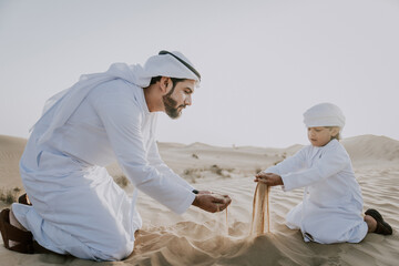 Wall Mural - Father and son spending time in the desert on a safari day. Arabian family from the emirates wearing the traditional white dress. Concept about lifestyle and middle eastern cultures