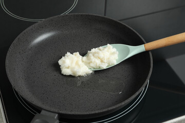 Frying pan with coconut oil and spoon on induction stove, closeup. Healthy cooking