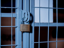 Locked Padlock Hangs On A Grid Door In The Basement.