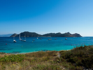 Canvas Print - Beautiful scene of rocky cliffs, plants and water with a blue sky in the Cies Islands, Spain