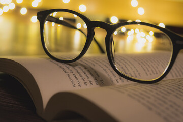 Canvas Print - Closeup shot of a reading glass on an opened book against bokeh lights