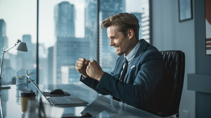 Excited Businessman in a Suit Sitting at a Desk in Modern Office, Using Laptop Computer. Successful Manager Ecstatic About Winning a Real Estate Investment Deal for Corporate Business.