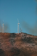 Sticker - Side view of rotating wind turbines against a blue sky on a sunny day