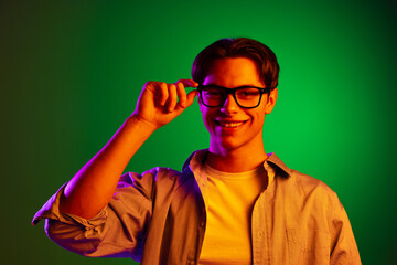 Wall Mural - Portrait of young smiling man putting eyewear isolated on green studio background in neon, monochrome.