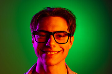 Wall Mural - Close-up face of young smiling man in modern eyewear isolated on green studio background in neon, monochrome.