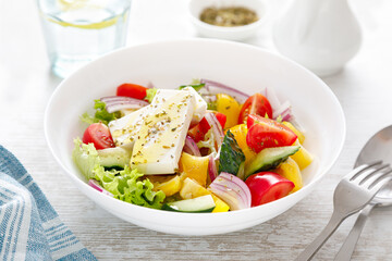 Fresh summer vegetable salad with lettuce, tomato, cucumber, bell pepper, onion and feta cheese, dressed with olive oil