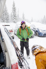 Man With Backpack And Skis Preparing In Snowy Parking Lot