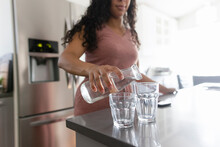 Woman Filling Glasses With Water At Kitchen Counter