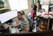 Man With Headphones Working From Home With Wife And Son In Background
