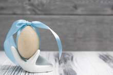 Wooden Egg With A Blue Ribbon In A Hand Shaped Egg Holder On A Wooden White Background.