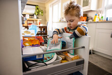 Cute Toddler Boy Reaching In Kitchen Drawer For Snacks