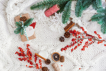 Wall Mural - Winter composition with  gifts, pine cones, cinnamon, candles on a light knitted blanket. Flat lay, top view. Warm cozy Christmas.