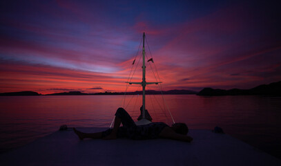 Silhuete of a young female lying on a ship on a sea background  at the purple sunset