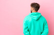 Young handsome caucasian man isolated on pink background in back position and looking back