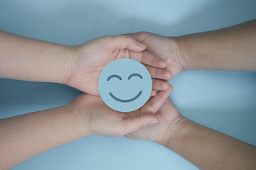 Wall Mural - 2 people hand holding blue paper cut happy smile face, positive thinking, mental health assessment , world mental health day concept	