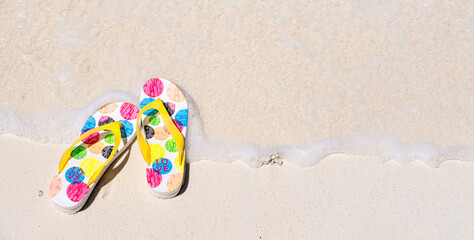 Wall Mural - Summer flop flops or sandals on sandy beach by sea water, top view, copy space