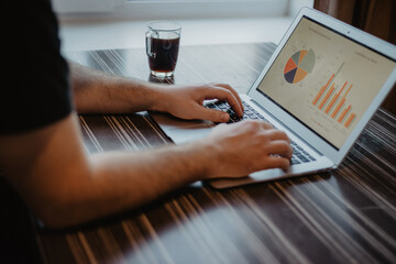 Canvas Print - Closeup shot of a person working on a financial report with his laptop at a coffee shop