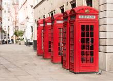Sunny United Kingdom Street Lined With Classic British Red Pay Phone Booths. The Kiosks Are A Cultural Icon Seen Streets Around London And Throughout England And Crown Dependencies.