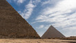 Two ancient Egyptian pyramids: Cheops and Chephren on a background of blue sky and clouds. The masonry walls are visible.  There are horse-drawn carts at the foot. Egypt