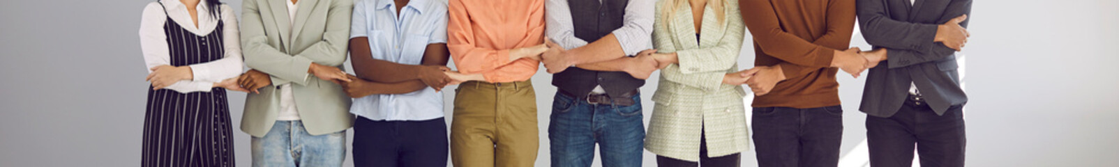 Banner with diverse team of young multiracial multiethnic business people standing together and holding hands, cropped midsection shot. Teamwork, cooperation, corporate unity, and synergy concepts