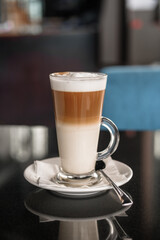 A glass of coffee latte on a table against a blurred background.