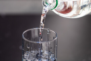 Canvas Print - Selective focus of pouring water from a clear plastic bottle into a glass on blurred background